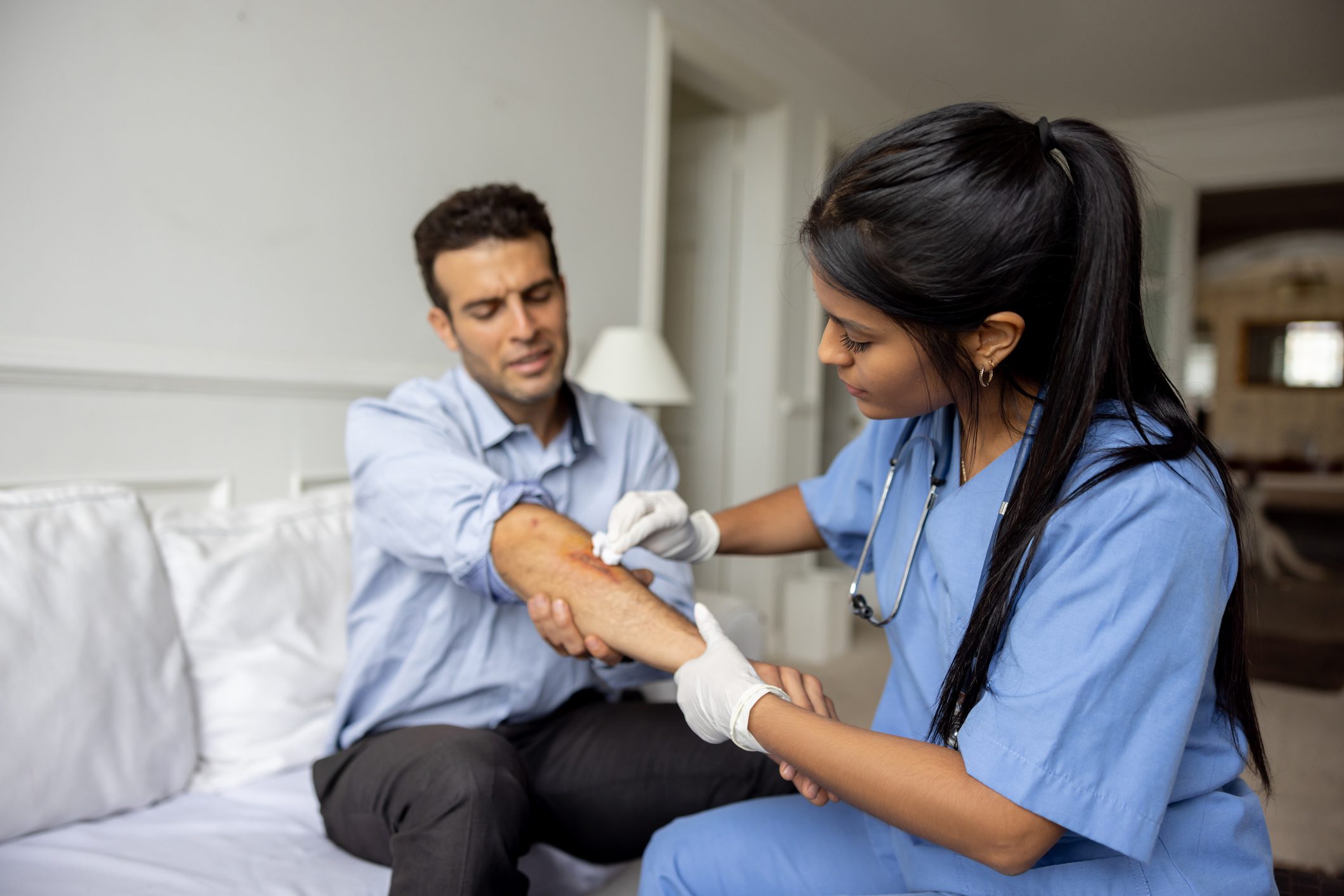 Nurse bandaging man's arm on couch.